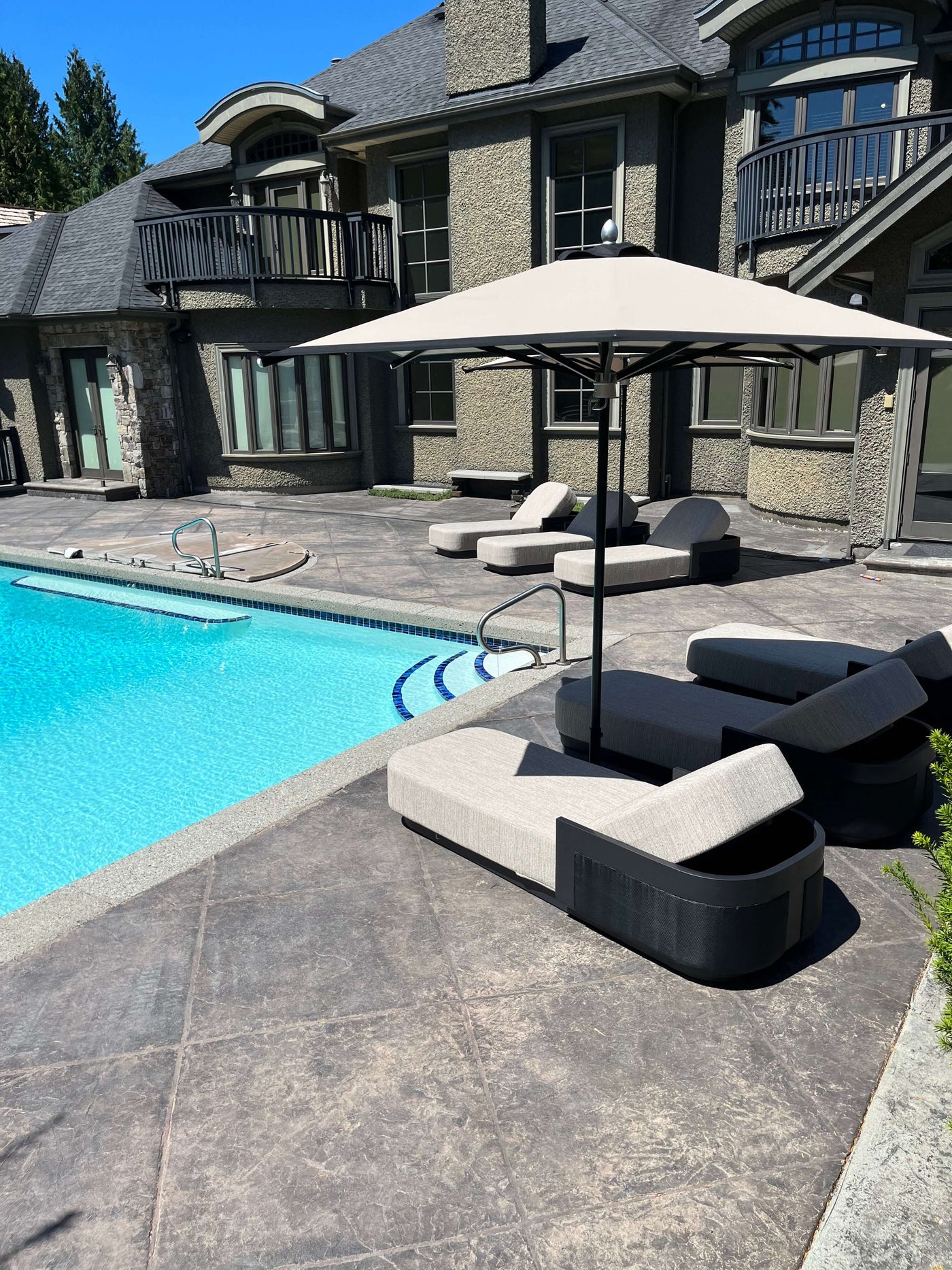 RM Sun Unbrella (stripe) 8x8 providing shade over poolside lounge chairs near a swimming pool.