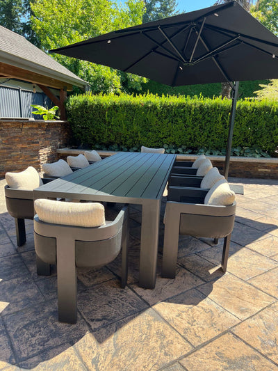 Aluminum outdoor dining chairs with cushions around a sleek table under a large umbrella in a garden setting.